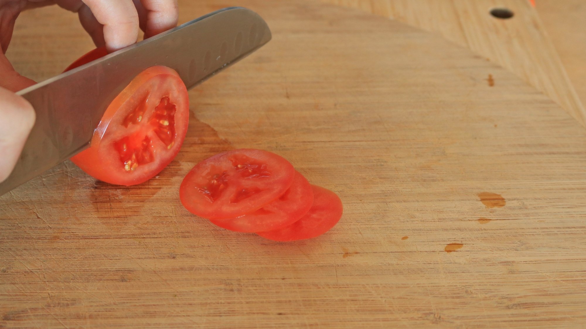 Un gros plan des mains d'une personne tranchant une tomate.