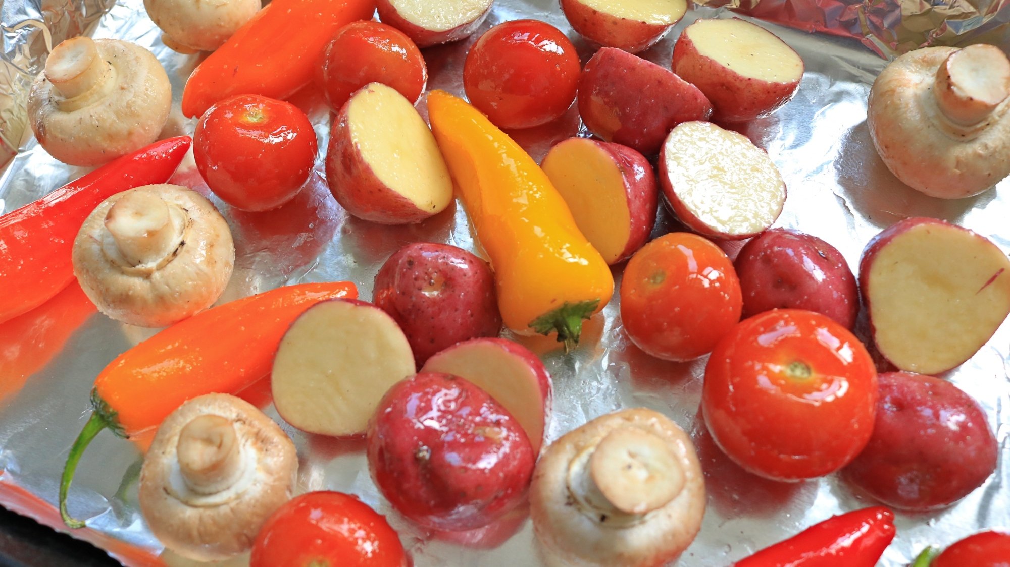 Différents légumes avec de l'huile et du sel sur une poêle doublée de papier d'aluminium.