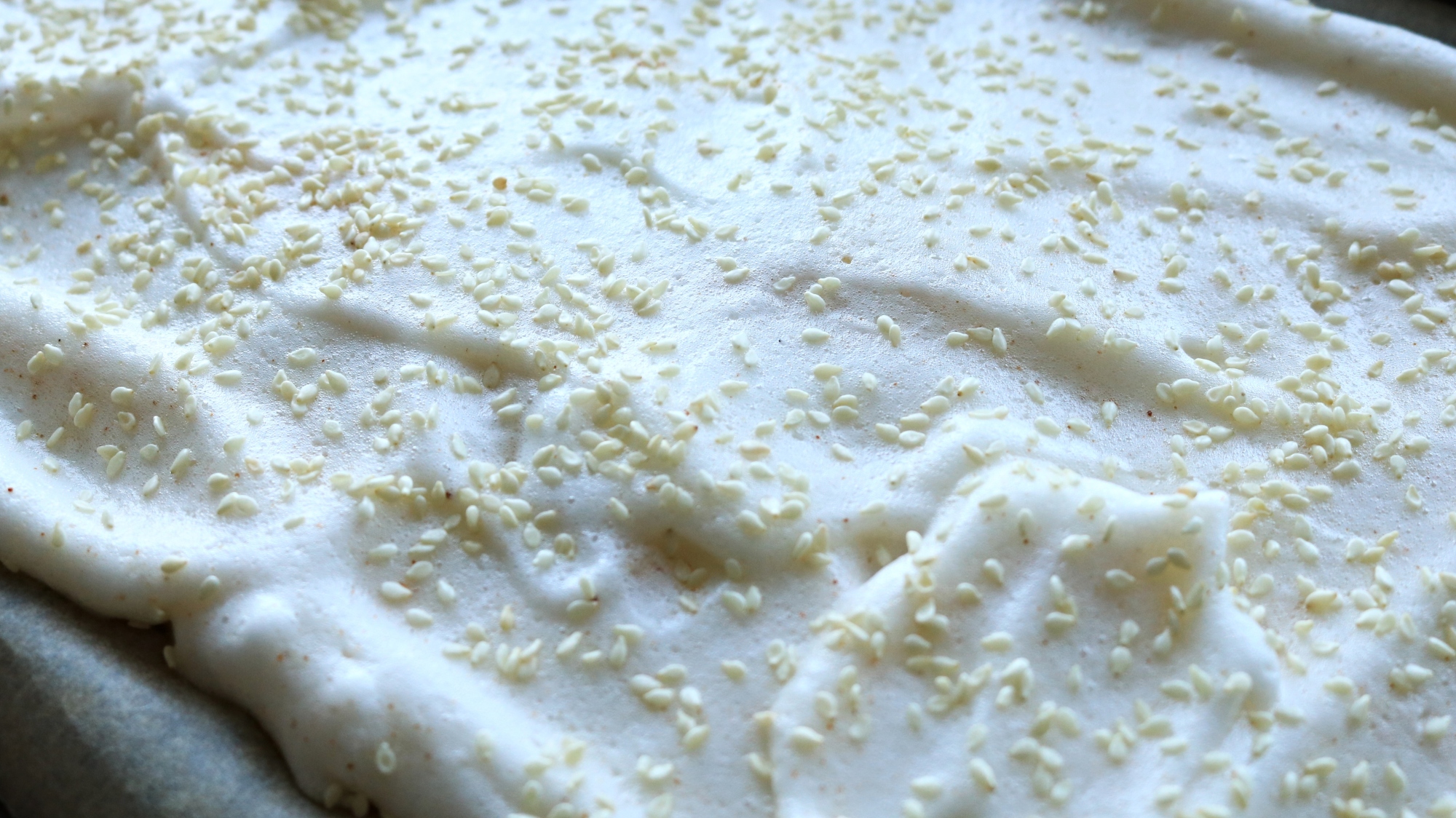 Meringue saupoudrée de graines de sésame réparties sur un plateau en feuille.