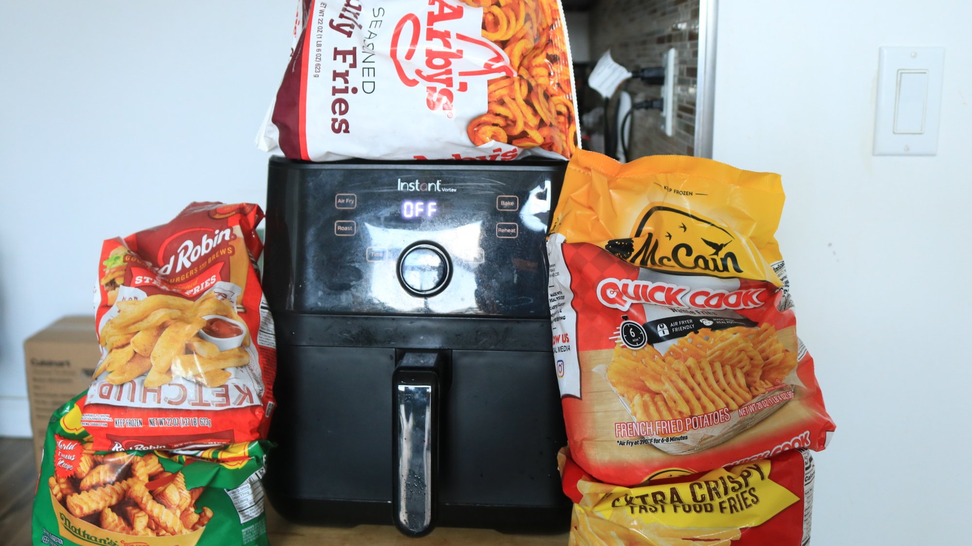 Des sacs de frites surgelées empilées autour d'une friteuse à air vortex instantanée.